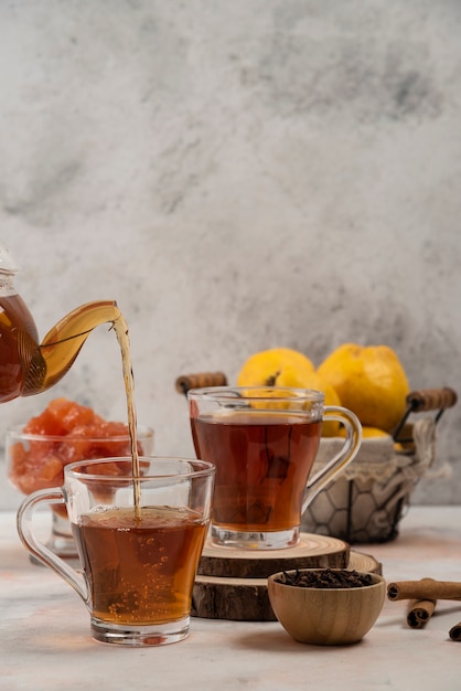 Tetera de vidrio transparente vierte té en taza de vidrio sobre mesa de mármol.