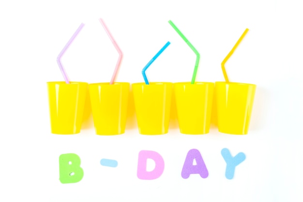 Foto gratuita texto de cumpleaños con vasos de plástico amarillo y coloridas pajas de beber