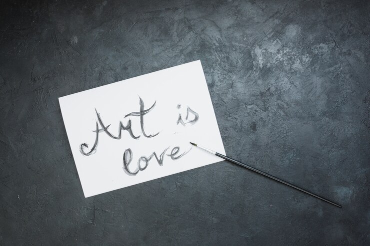 Foto gratuito texto escrito a mano "el arte es amor" en papel blanco con pincel sobre superficie de pizarra