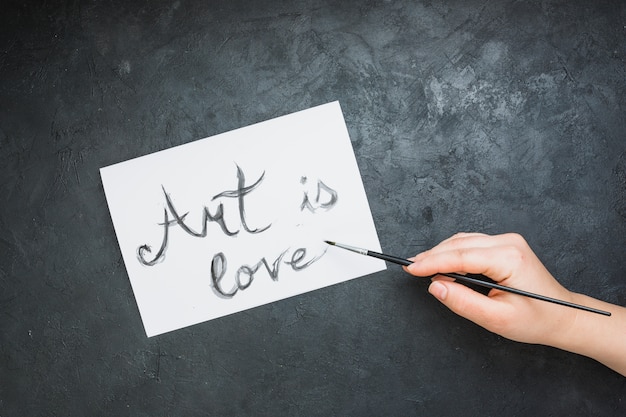 Texto escrito a mano de la mujer &quot;el arte es amor&quot; en papel blanco con pincel sobre fondo de pizarra