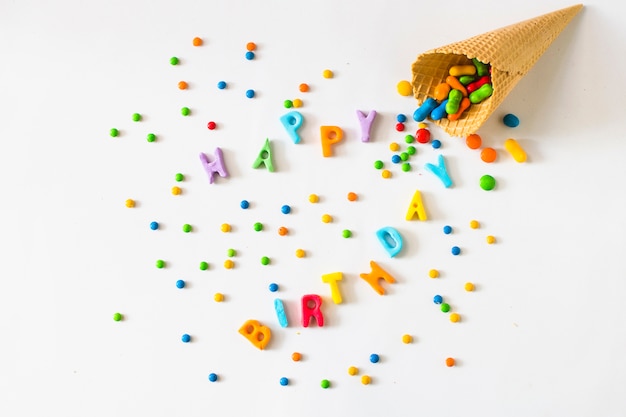 Texto feliz día de nacimiento con caramelos que se derraman desde el cono de helado de waffle