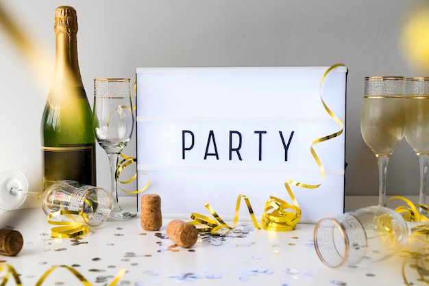 Texto de fiesta en caja de luz con botella de champán y artículos decorativos