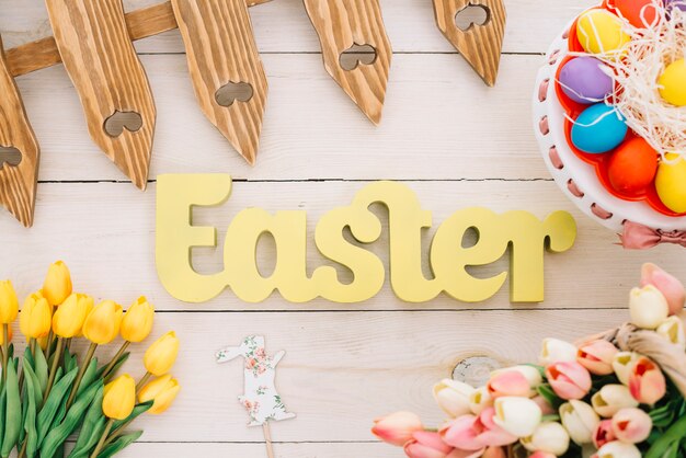 Texto de pascua con valla; apoyo de conejo; Tulipanes y coloridos huevos de Pascua en cakestand en escritorio