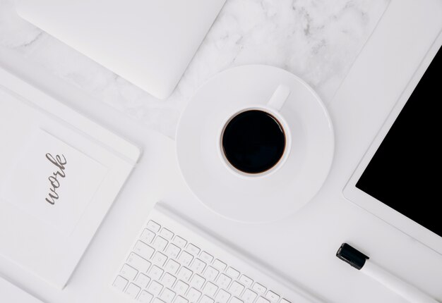 Texto de trabajo en diario; tableta digital; taza de café; Teclado y marcador negro en el escritorio blanco.