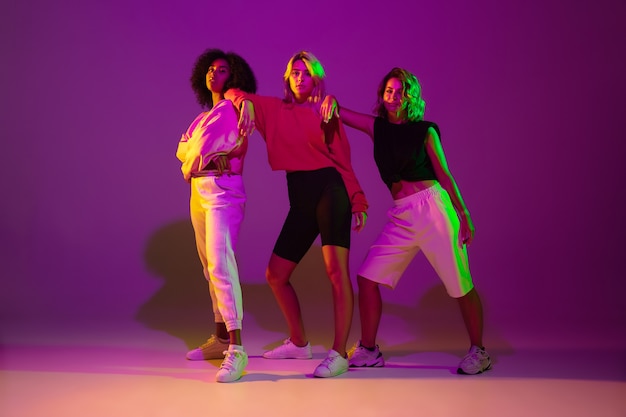 Tiempo de bailar. Hombres y mujeres con estilo bailando hip-hop en ropa brillante sobre fondo verde en el salón de baile con luz de neón.