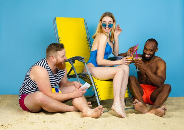 Tiempo brillante. Amigos felices descansando, bebiendo cócteles sobre fondo azul de estudio. Concepto de emociones humanas, expresión facial, vacaciones de verano o fin de semana. Frío, verano, mar, océano, alcohol.