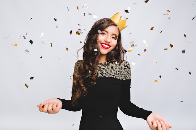 Tiempo feliz, joven sonriente celebrando el año nuevo, con vestido negro y corona amarilla, fiesta disco de carnaval feliz, confeti brillante, divirtiéndose, sonriendo.