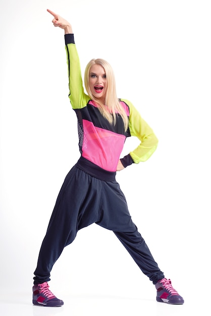 Tiempo de moverse. Foto de estudio de longitud completa vertical de una alegre bailarina rubia en ropa deportiva gritando emocionada con su brazo levantado en el aire aislado