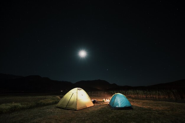 Tiendas turísticas en campamento entre prado en las montañas de noche