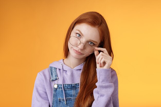 Tienes que estar bromeando. Pelirroja molesta, inteligente, irritada, hermana mayor, mirada de debajo de la frente, quitarse las gafas, enrollar los párpados, sonrisas burlonas, molestas, enojadas, estúpidas, de pie, fondo naranja.