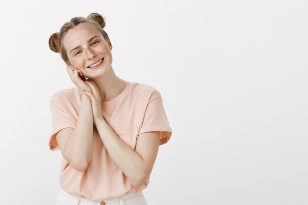 Tierna adolescente sonriente posando contra la pared blanca