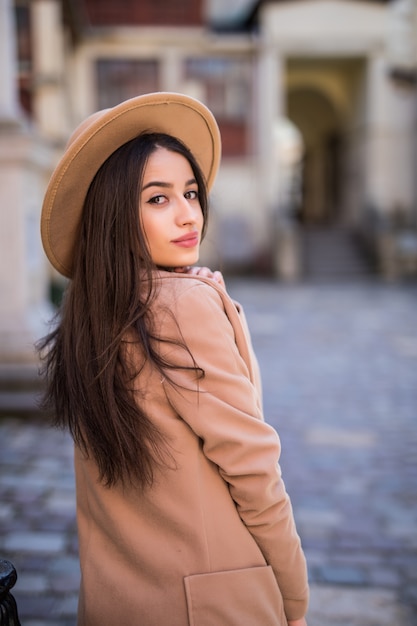 Tierna dama sonriente está caminando por la calle y posando en casual abrigo moderno y sombrero