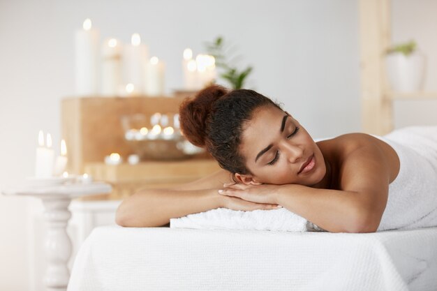 Tierna mujer africana descansando relajante con los ojos cerrados en el salón de spa.