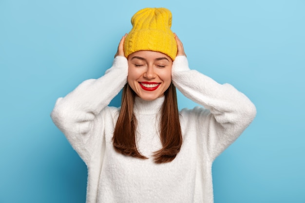 Tierna mujer europea con una sonrisa suave, mantiene ambas manos en la cabeza, tiene un mareo agradable, usa maquillaje