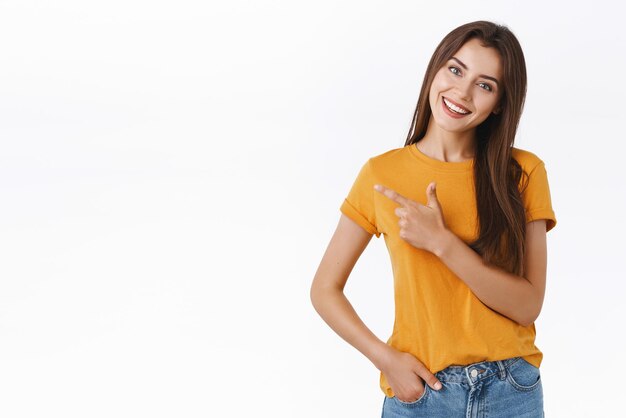 Tierna mujer femenina y encantadora en camiseta amarilla inclina la cabeza y sonríe tontamente mientras da consejos donde comprar el viernes negro apuntando a la esquina superior izquierda de pie encantado y feliz recomendar promoción