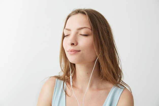 Tierna niña bonita sonriendo con los ojos cerrados escuchando música en auriculares.