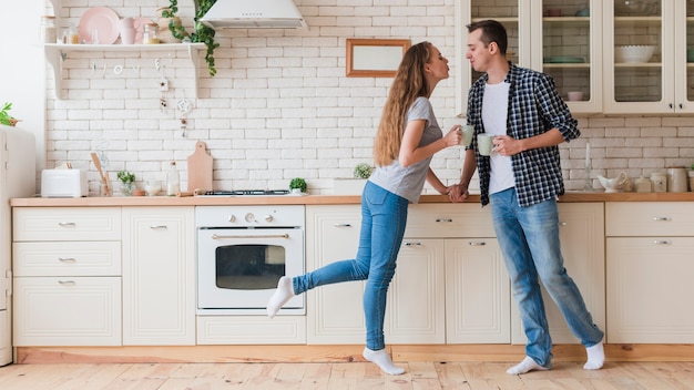 Tierna pareja bebiendo té y de pie en la cocina