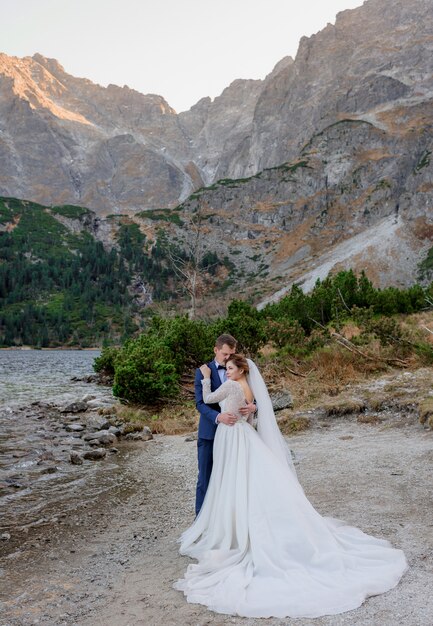 Tierna pareja de novios está de pie en el pintoresco paisaje de las altas montañas de otoño