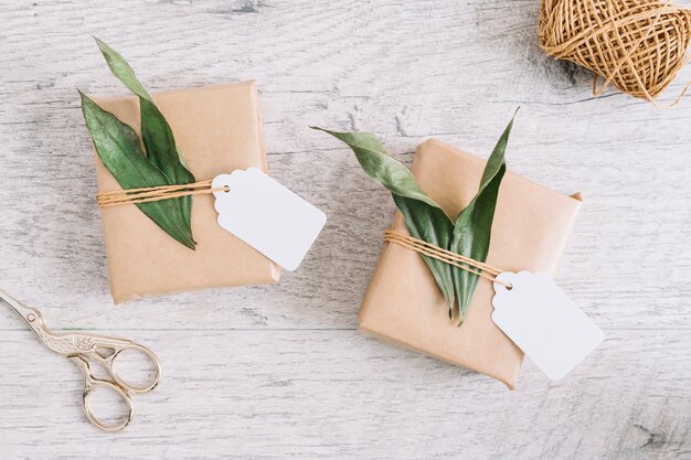 Tijeras y regalos envueltos con etiqueta y hojas sobre fondo de madera