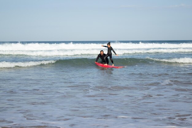 Útil padre e hija haciendo deportes en la playa. Hombre adulto medio enseñando a una niña de pelo oscuro cómo andar en tabla de surf. Familia, ocio, concepto de estilo de vida activo.
