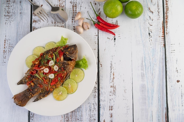 Tilapia frita con salsa de chile, ensalada de limón y ajo en un plato sobre un fondo blanco de madera