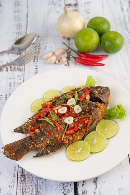 Tilapia frita con salsa de chile, ensalada de limón y ajo en un plato sobre una mesa de madera blanca.