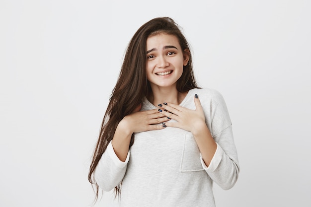 Tímida linda mujer adolescente con el pelo largo y liso oscuro sonriendo alegremente. Emociones positivas, sentimientos y expresiones faciales.