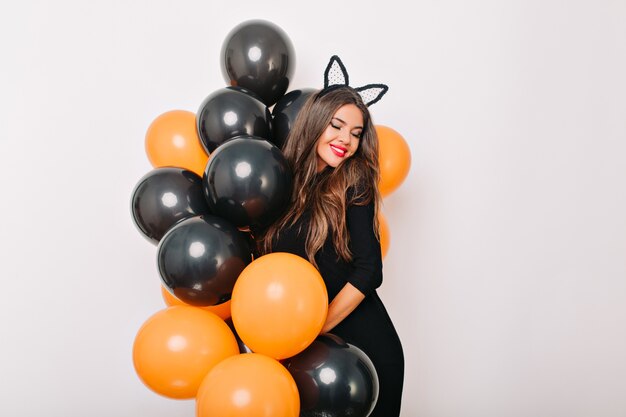 Tímida mujer de pelo largo posando con coloridos globos de halloween