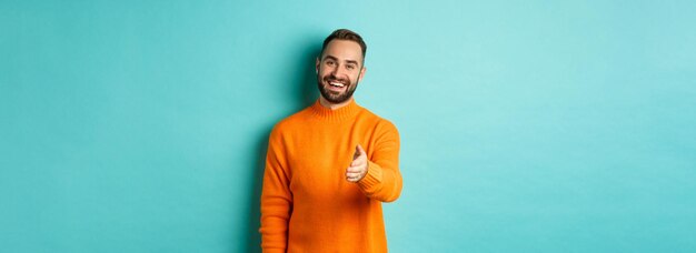 Un tipo amable y agradable extiende la mano para saludarte y saludarte sonriendo diciendo hola de pie sobre la luz