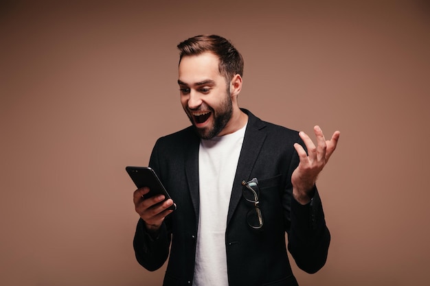 El tipo con camiseta y chaqueta mira felizmente el teléfono inteligente