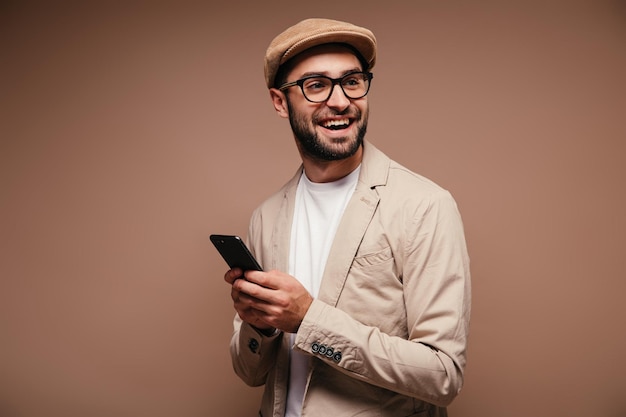 El tipo con chaqueta brillante y anteojos sonríe y sostiene el teléfono inteligente