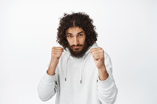 Un tipo serio listo para pelear con los puños cerrados levantados en una pose de boxeo defendiéndose en una pose de luchador de pie sobre fondo blanco