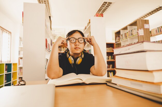 Tirado del estudiante asiático joven que se sienta en la tabla. Estudiante joven que estudia en biblioteca.