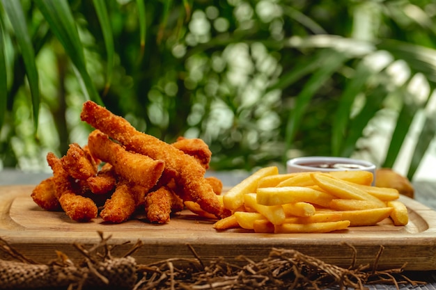 Tiras de pechuga de pollo empanadas fritas con salsa de tomate y papas fritas en una tabla de madera