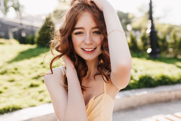 Tiro al aire libre de la increíble chica de jengibre con peinado rizado escalofriante en el parque. Preciosa modelo de mujer sonriente posando en la naturaleza.