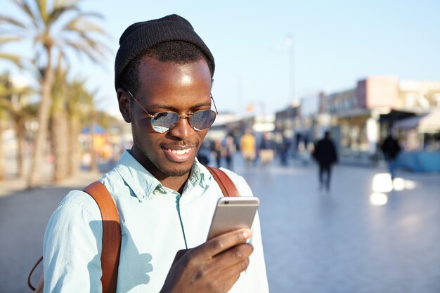 Tiro al aire libre de sonriente joven viajero alegre con smartphone