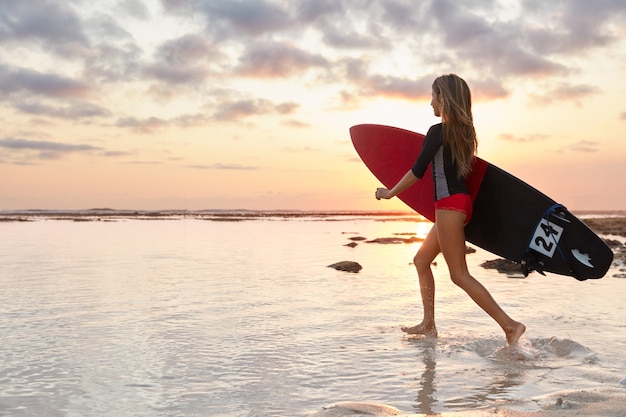 Foto gratuita tiro al aire libre de surfista deportivo se ejecuta en el agua del océano, tiene piernas delgadas