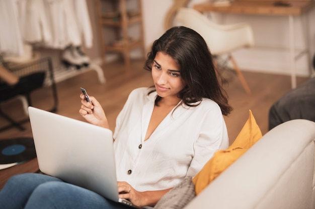 Tiro de alta vista de mujer sosteniendo una tarjeta de crédito y usando su laptop