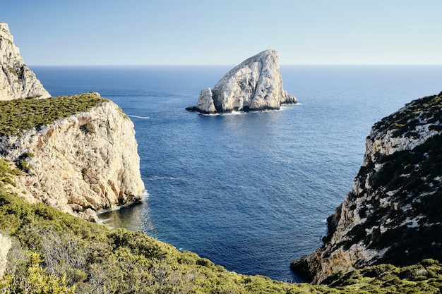 Tiro de alto ángulo de acantilados cubiertos de hierba cerca del mar con una roca en la distancia
