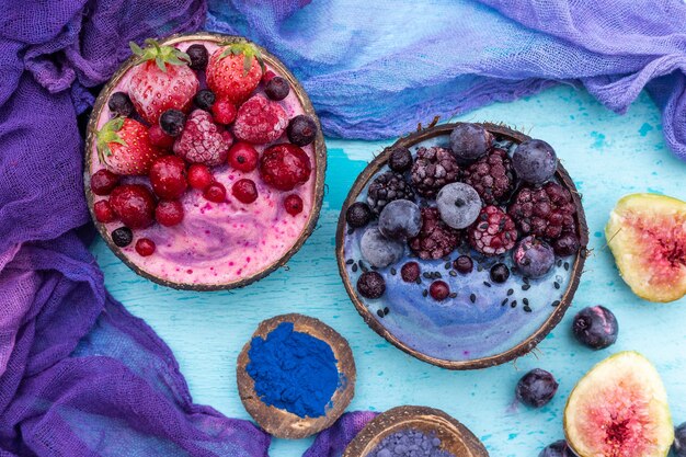 Tiro de alto ángulo de deliciosos batidos de frutas cubiertos con frutas congeladas en tazones de coco