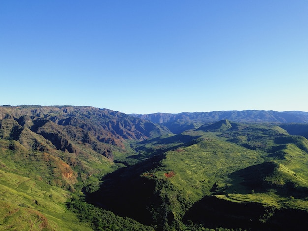 Foto gratuita tiro alto ángulo de las magníficas montañas cubiertas de árboles bajo el cielo azul