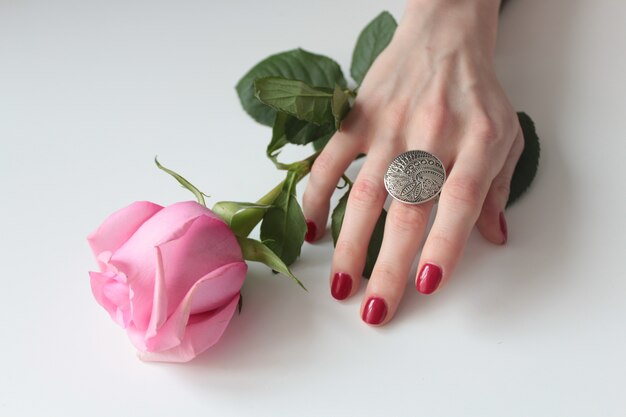 Tiro de alto ángulo de una mano femenina con un hermoso anillo de plata en una rosa con hojas verdes