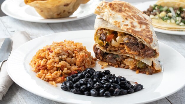 Tiro de ángulo alto de arroz con especias, frijoles negros y sándwiches de carne en un plato sobre una superficie de madera