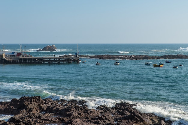 Tiro de ángulo alto de los barcos en el mar cerca del muelle y la orilla rocosa