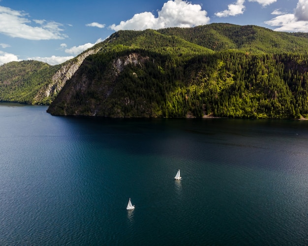 Foto gratuita tiro de ángulo alto de barcos navegando en el agua con montañas boscosas en la distancia