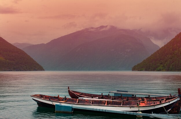 Tiro de ángulo alto de barcos oxidados en el mar cerca de altas montañas durante la puesta de sol en Noruega