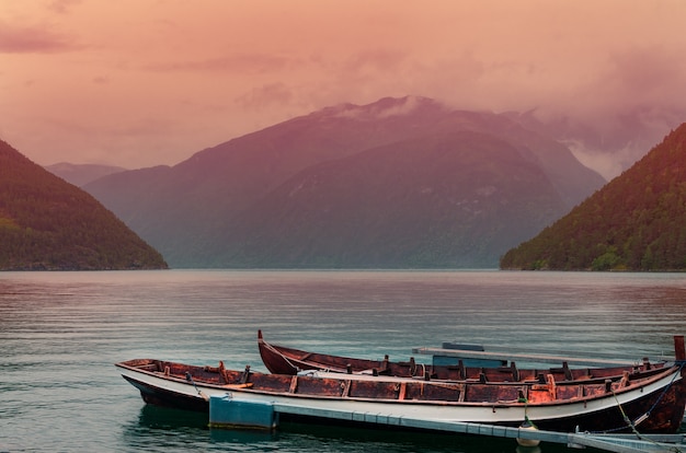 Tiro de ángulo alto de barcos oxidados en el mar cerca de altas montañas durante la puesta de sol en Noruega