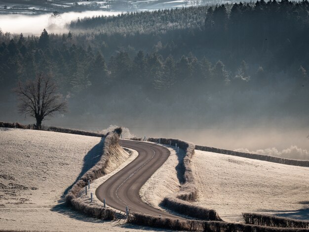 Tiro de ángulo alto de una carretera con curvas en medio de campos nevados con colinas boscosas