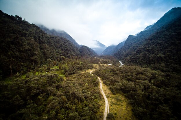 Tiro de ángulo alto de una carretera rodeada de árboles verdes y montañas con un cielo nublado