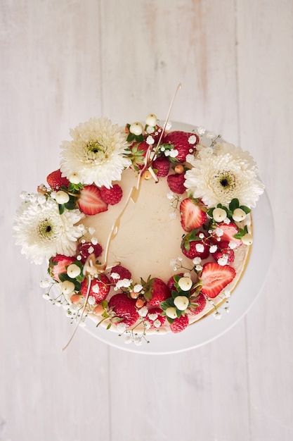 Tiro de ángulo alto de delicioso pastel de bodas blanco con frutos rojos y flores en la mesa de madera blanca
